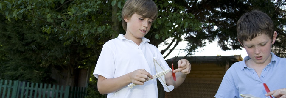 Children winding rubber bands on model helicopters