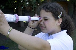 Young girl looking through a cardboard tube telescope