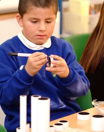 Young boy making a cardboard tube telescope in a classroom