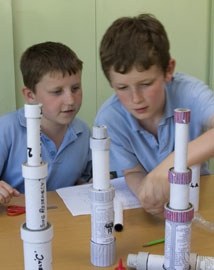 Two young boys making a cardboard tube telescope in a classroom